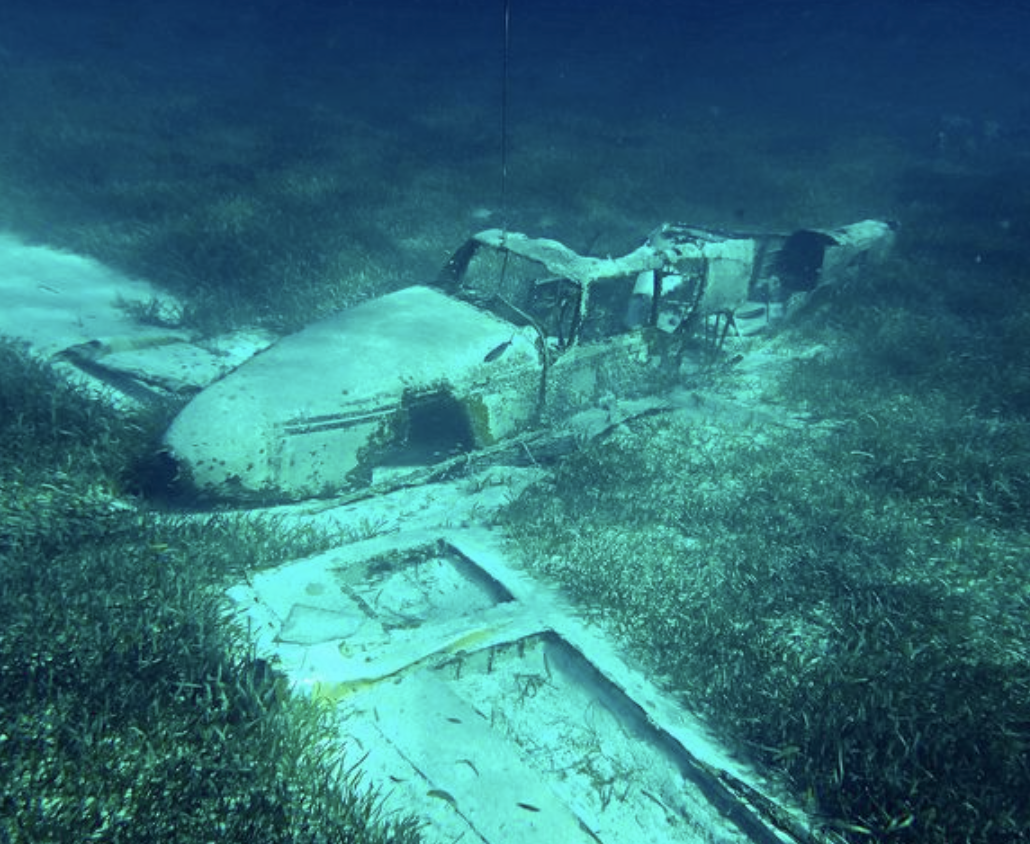A very old-looking plane sitting on the bottom of a body of water with parts of the plane missing