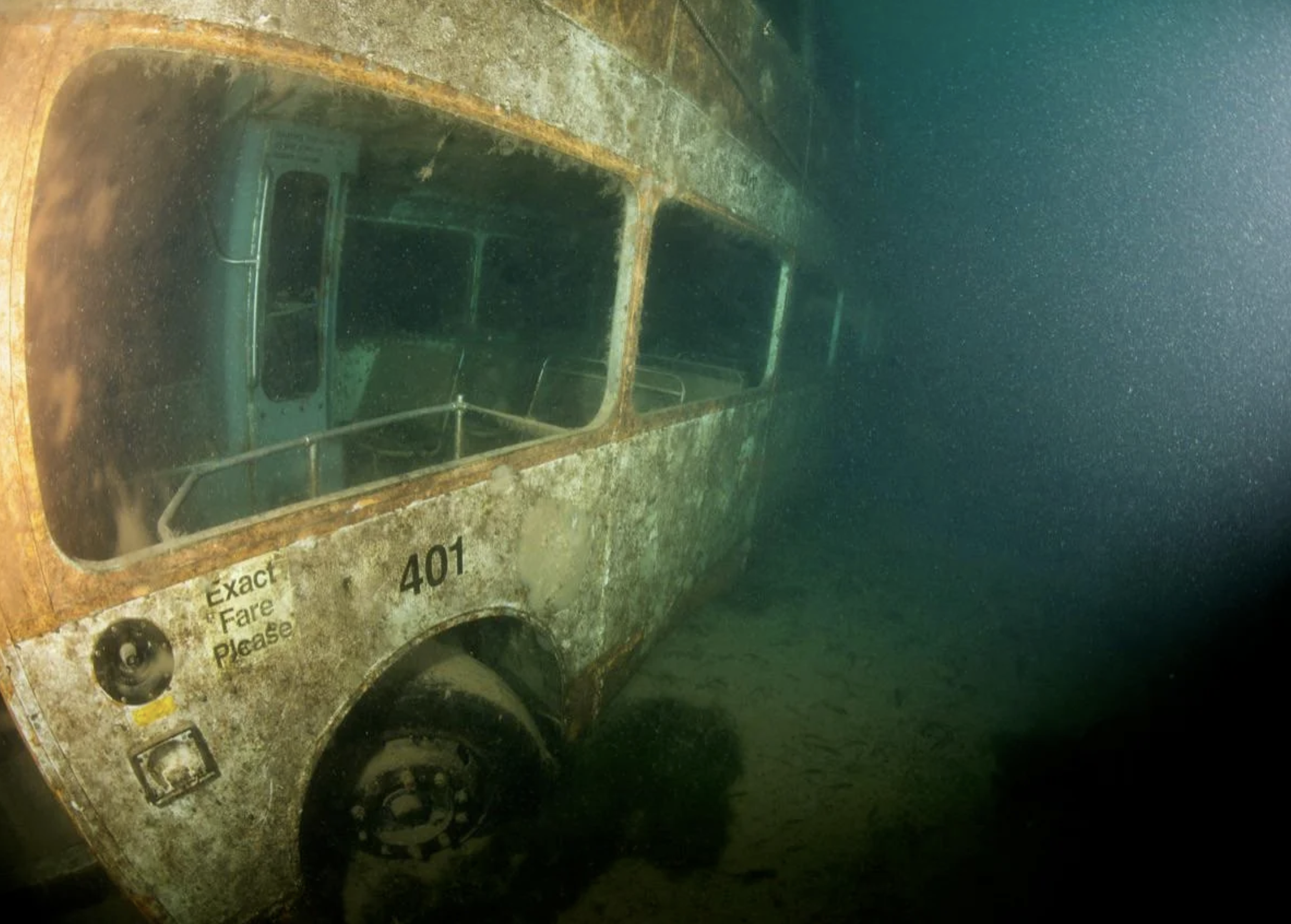 A bus sitting on the bottom of the ocean, covered in algae