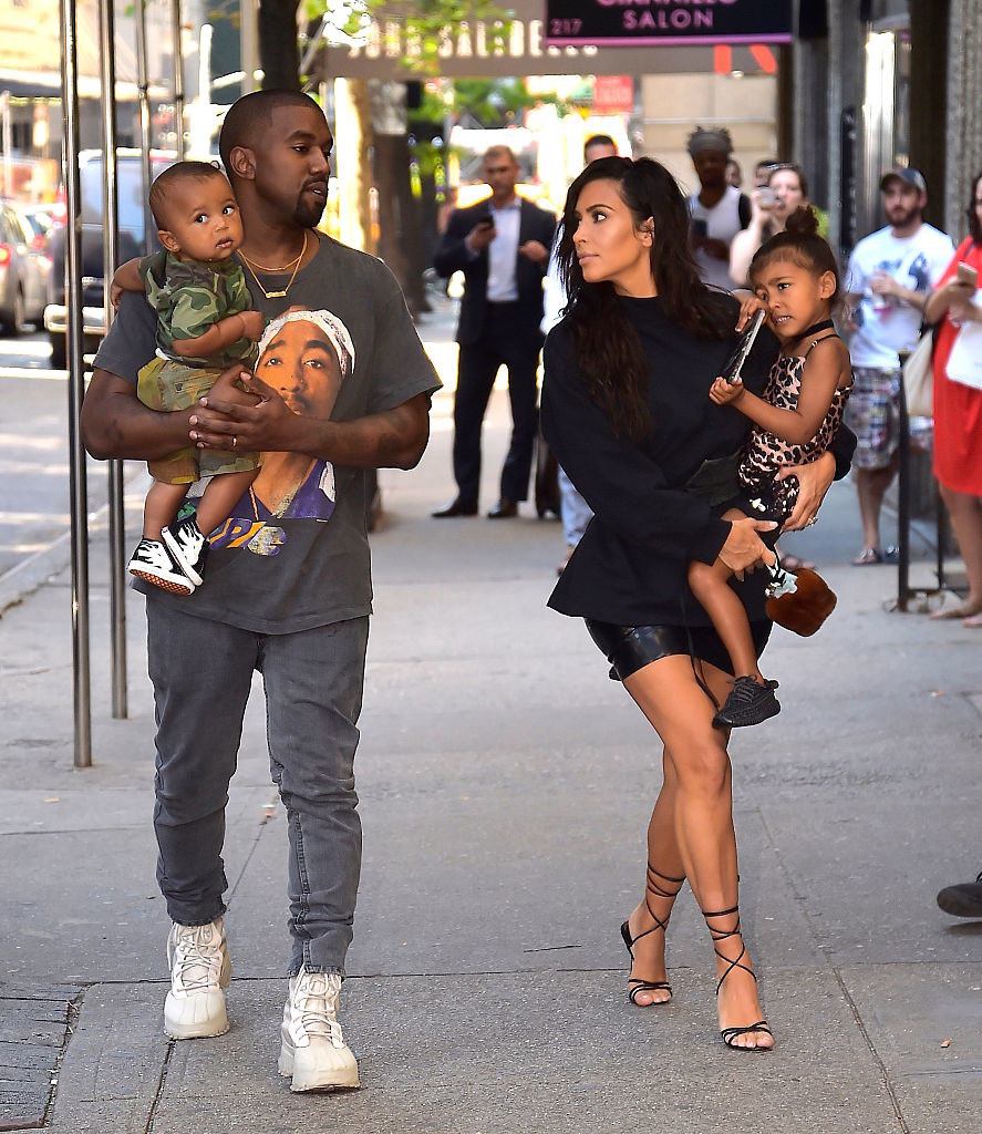 kim and kanye walking outside holding two of their kids