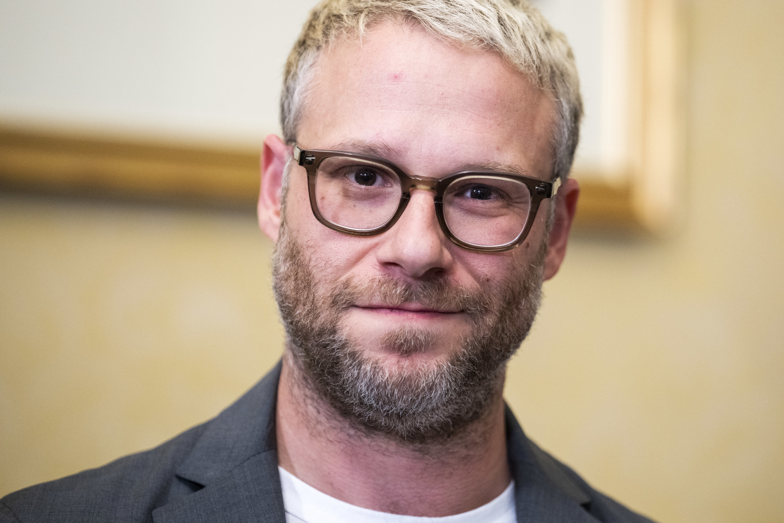 Close up of Seth&#x27;s head and shoulder; he smiles and wears thick rimmed glasses, and his hair is bleached