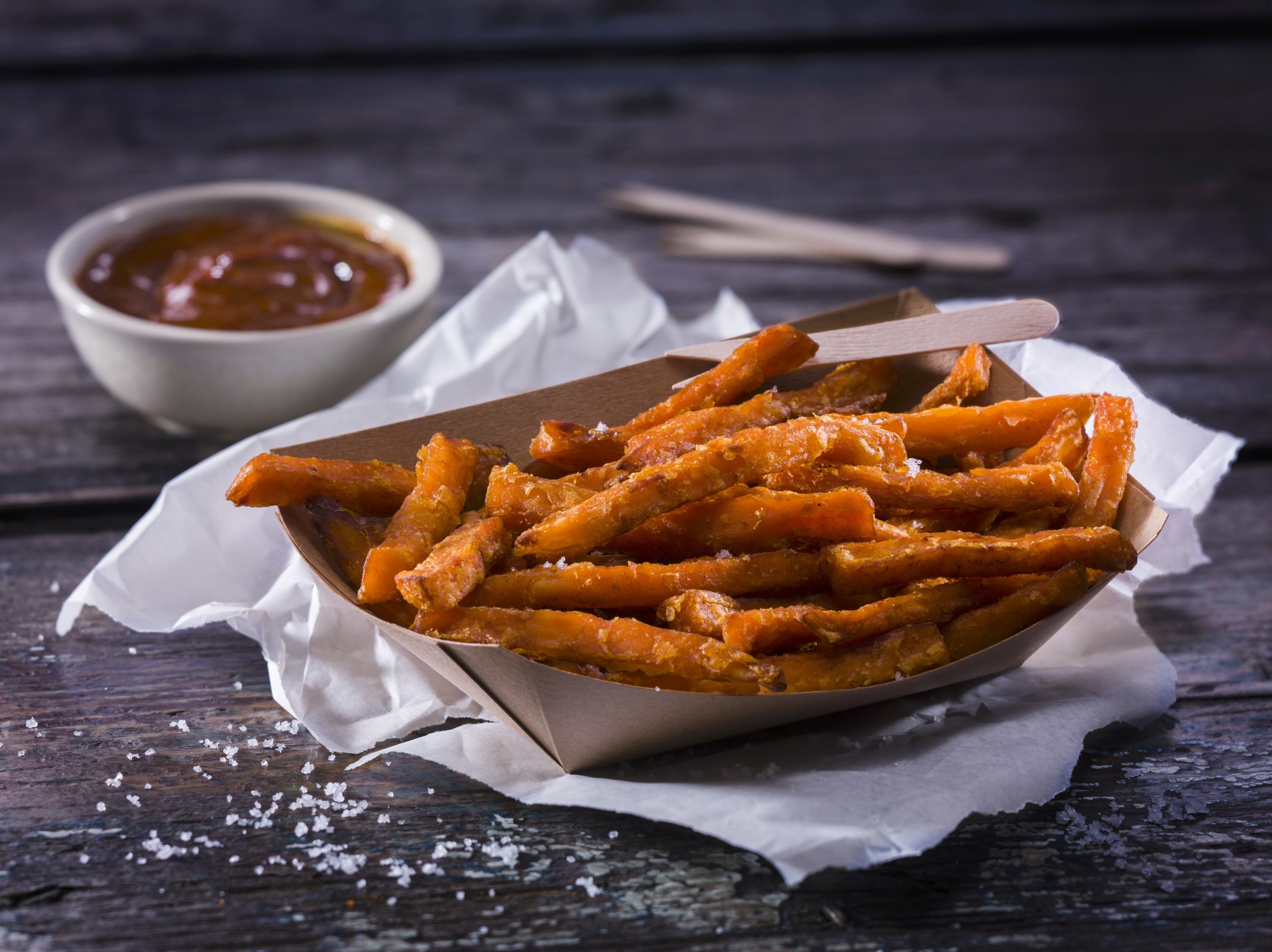 A basket of sweet potato fries on top of a white napkin, a side dish a barbecue sauce