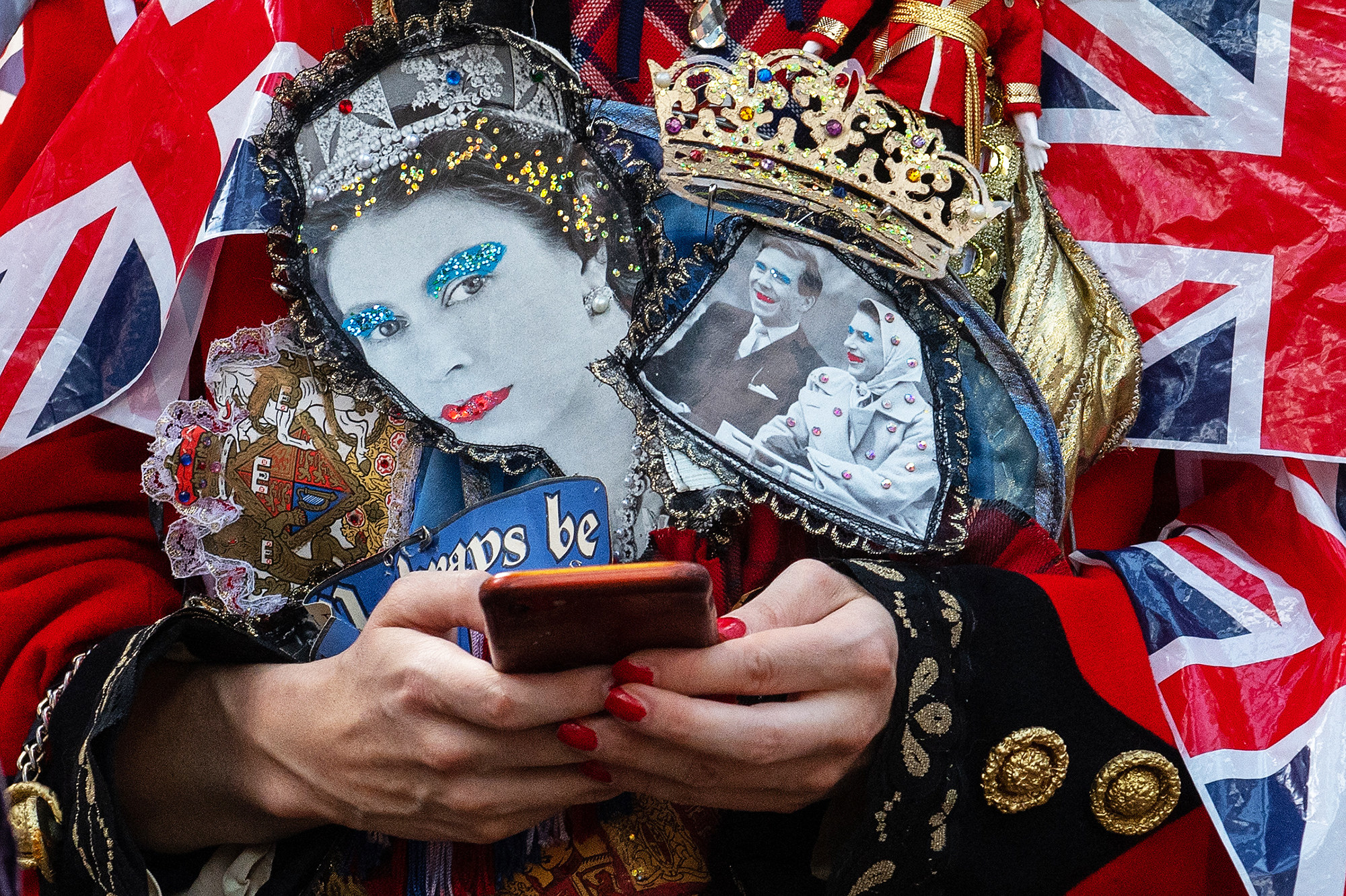 Person holding a cellphone wears clothing that includes bedazzled images of the Queen&#x27;s face