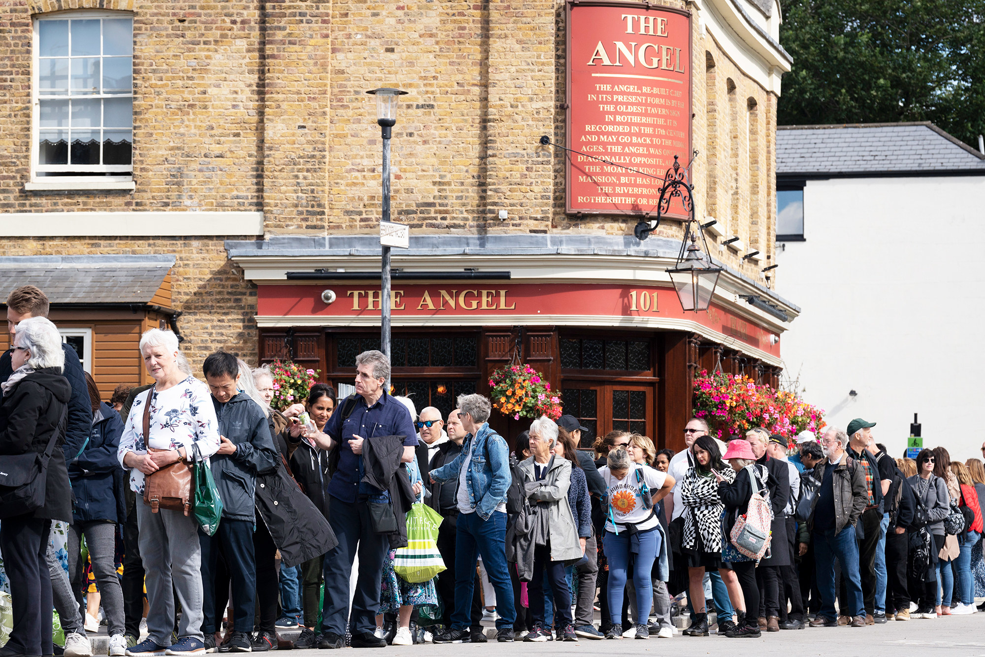A line of people stand outside the Angel tavern