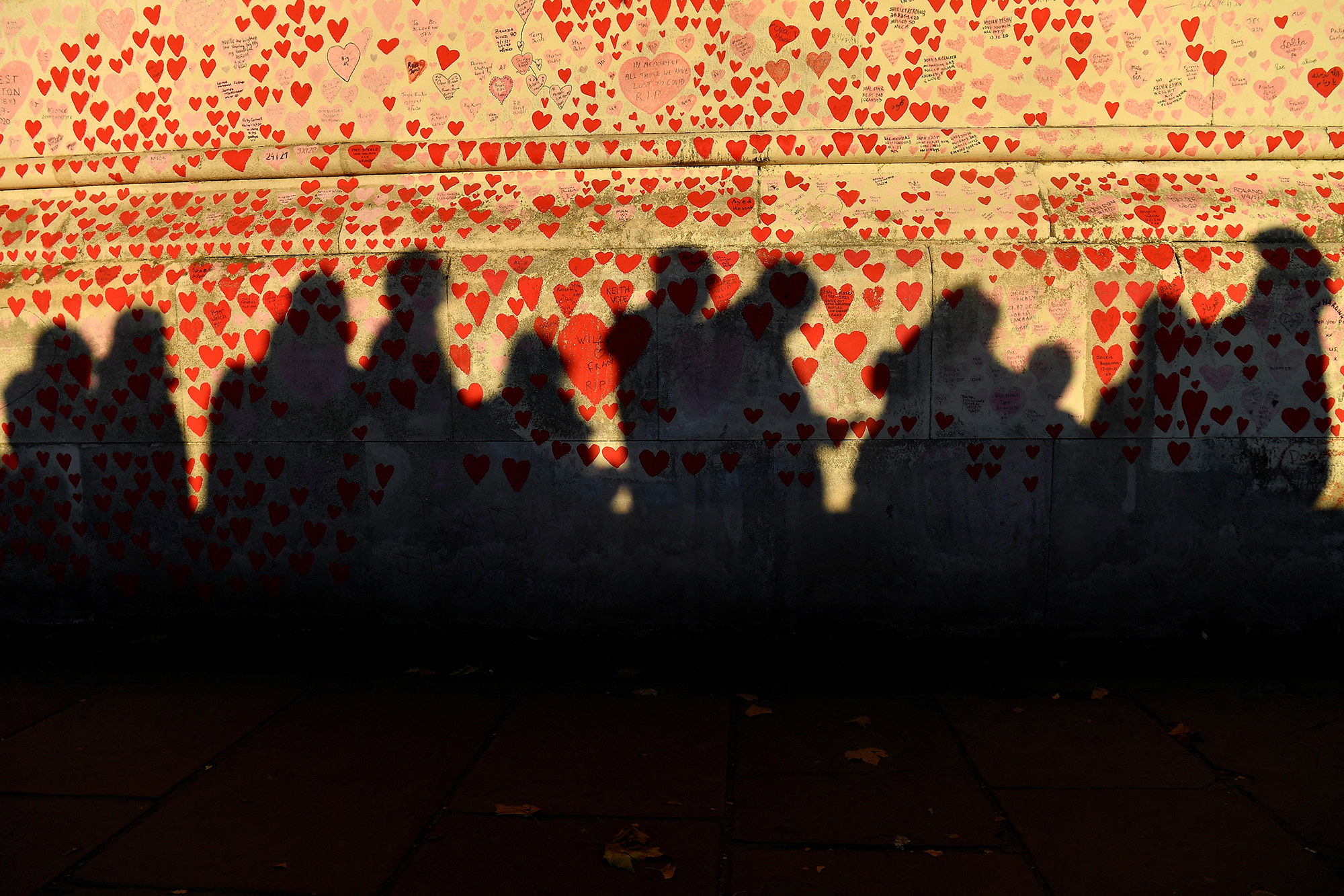 Shadows of people in the queue are reflected on a wall covered with heart drawings and messages