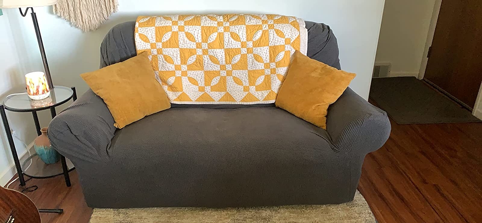 Reviewer image of couch with gray cover on it and yellow throw pillows and blanket