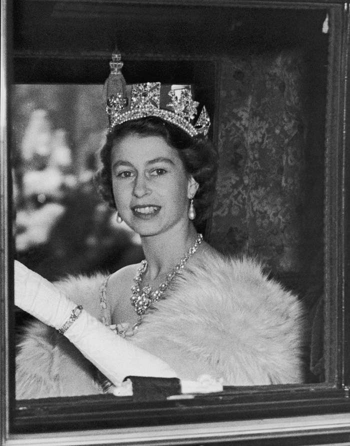 The Queen in a vehicle wearing a tiara and jewel-encrusted necklace