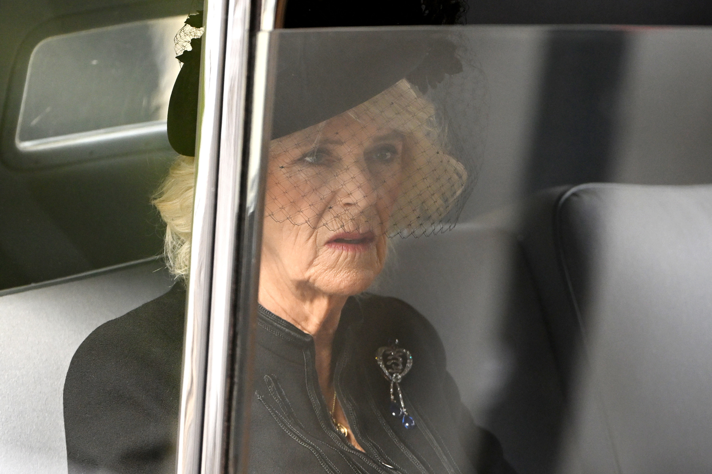 Queen Camilla in a black dress and hate sitting in a car as she leaves Westminster Abbey