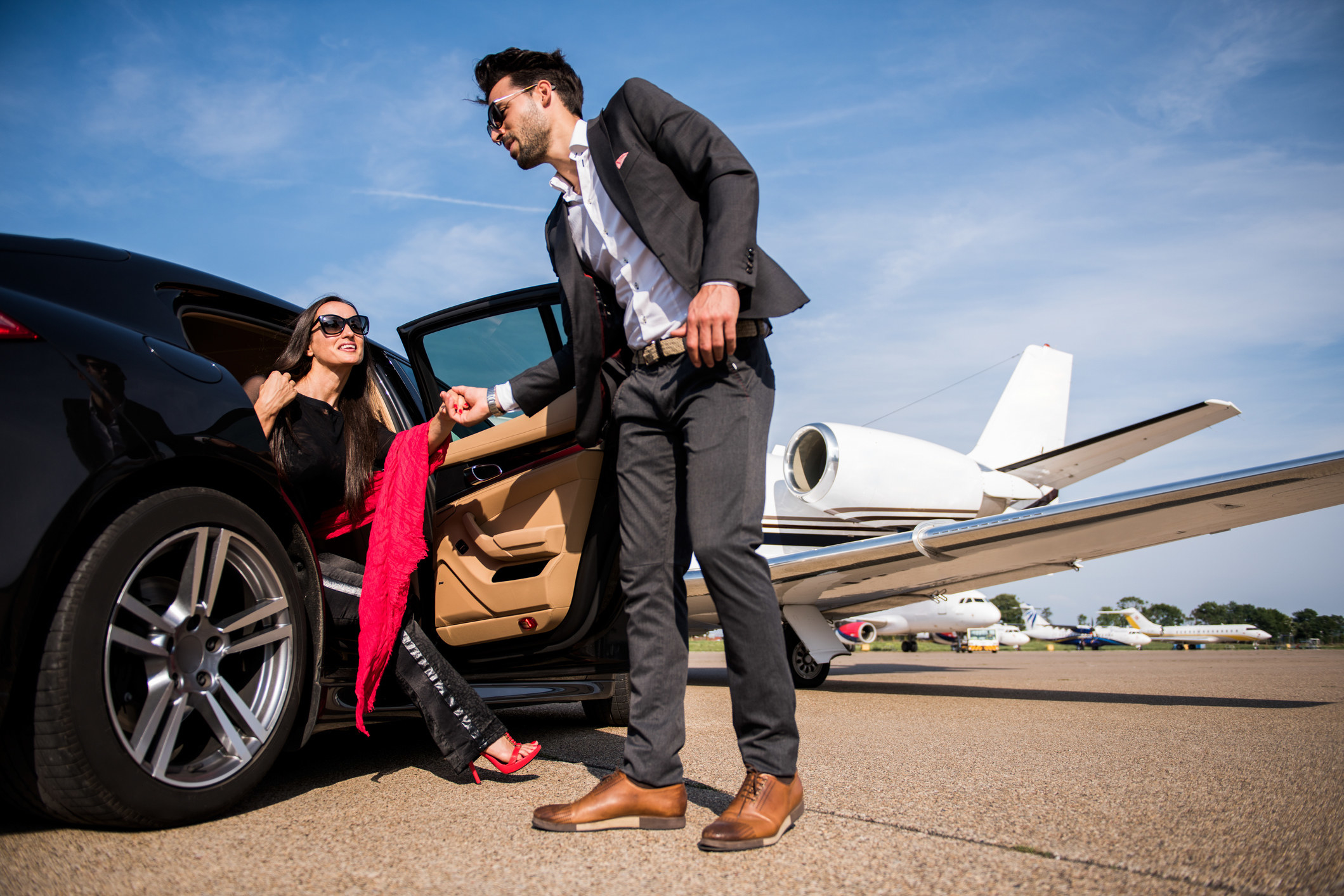 A man helping a woman exit a car on the tarmac