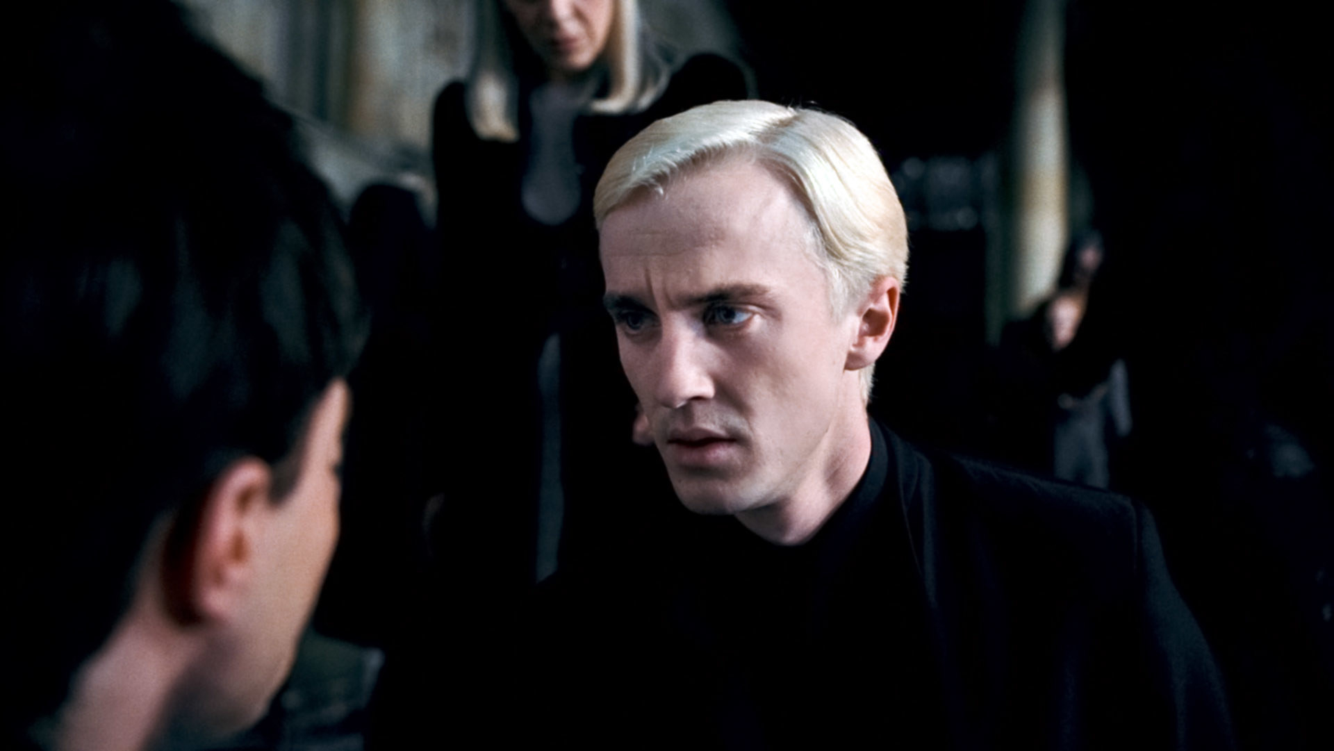 Drace with slicked-back blonde hair and a wand in his face
