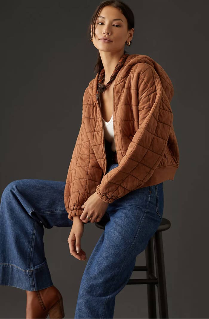 model wearing rust orange quilted jacket sitting on a stool