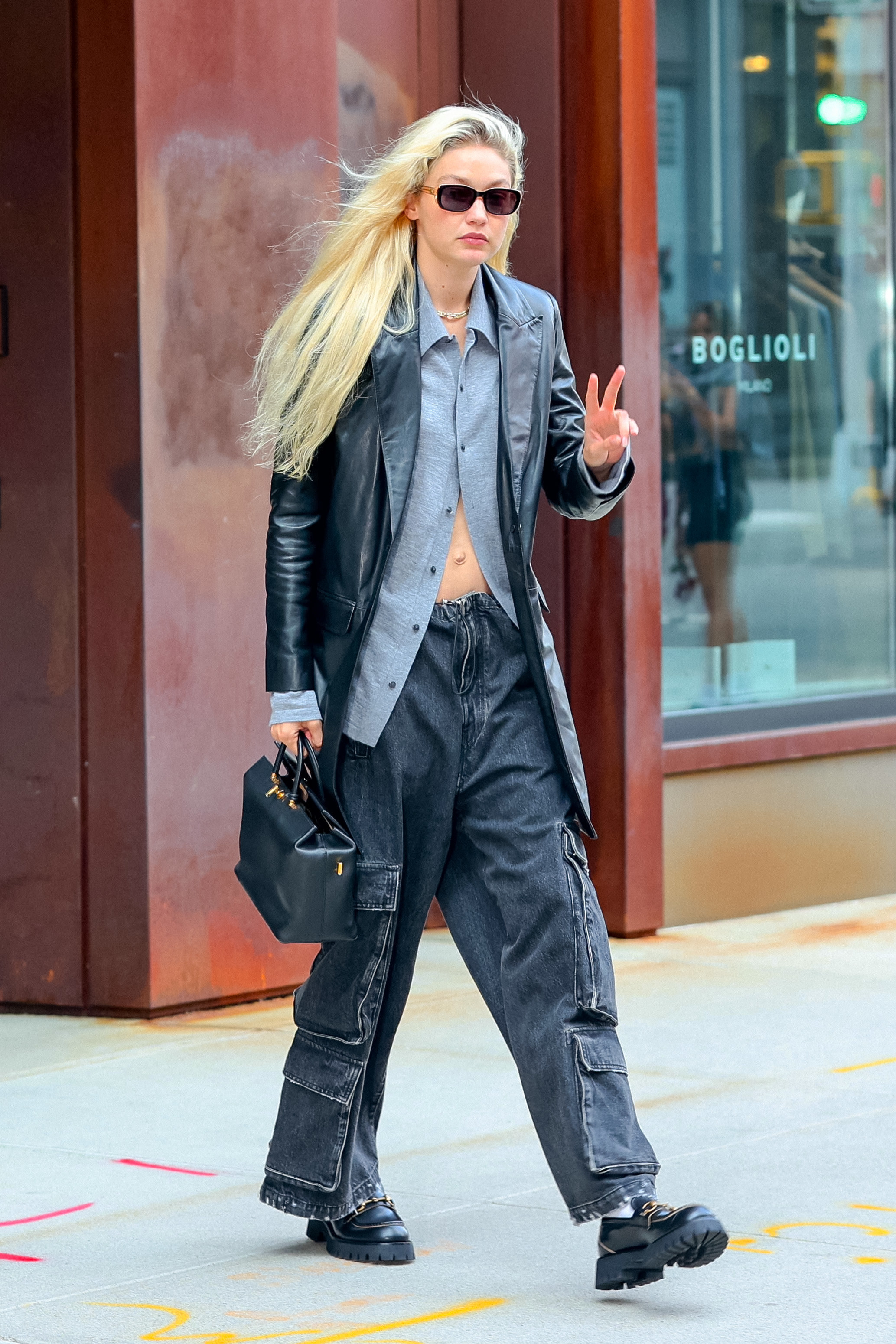 Gigi in loose cargo jeans and a jacket and giving the peace sign