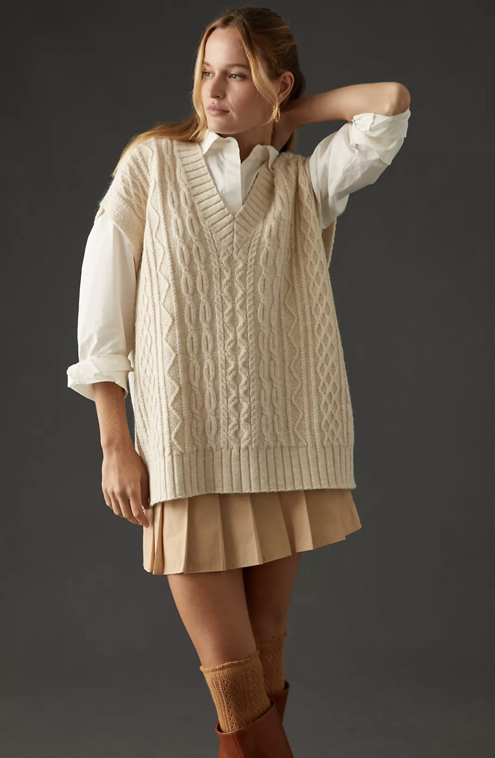 model wearing the cream vest over a shirt with a skirt and boots