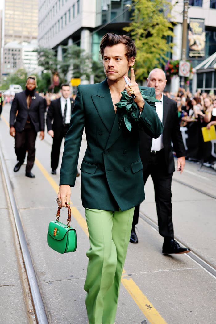 Harry in a green suit and walking with a small handbag
