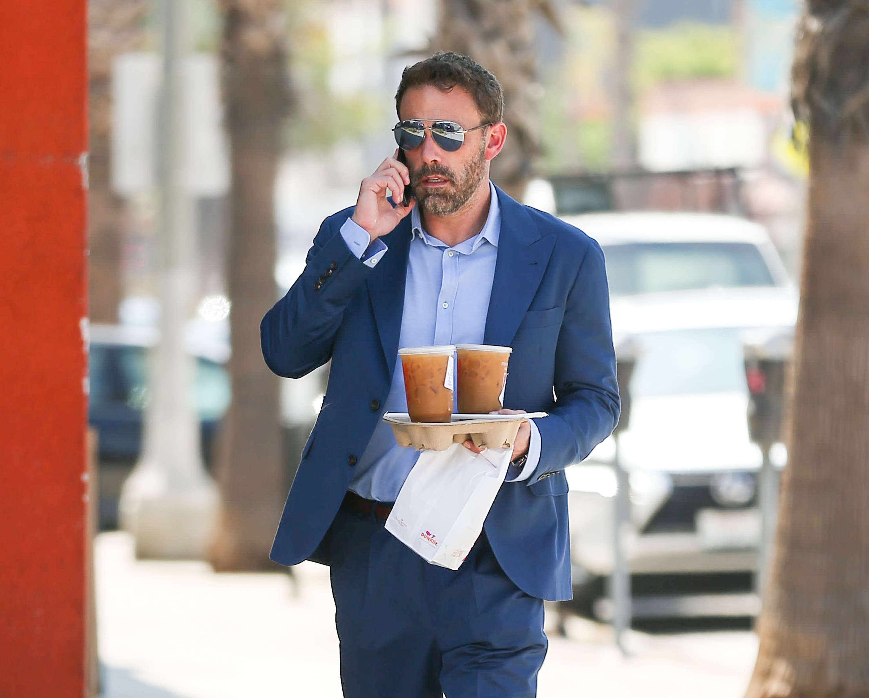 Ben on the phone and holding a takeout tray with two coffees in it