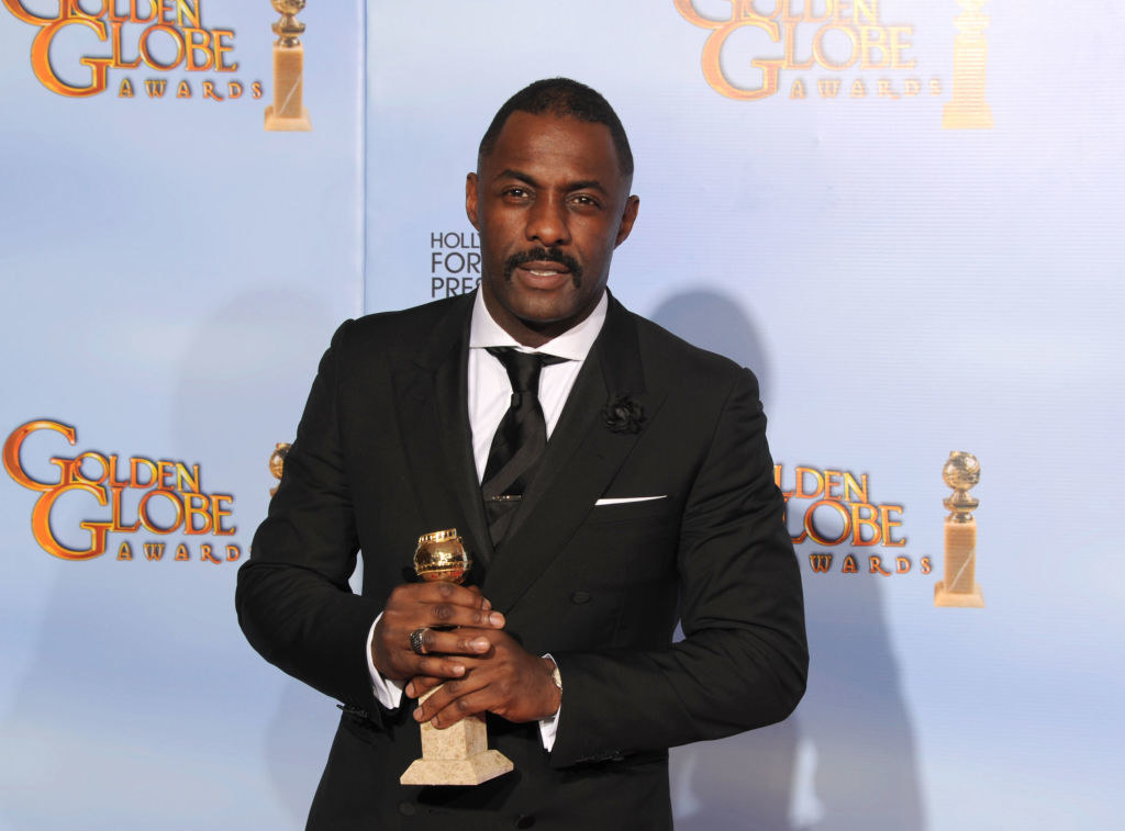 Idris in a suit holding a Golden Globe