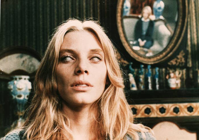 A blonde blind woman stands ominously before an extravagant wall and mirror in "The Beyond"