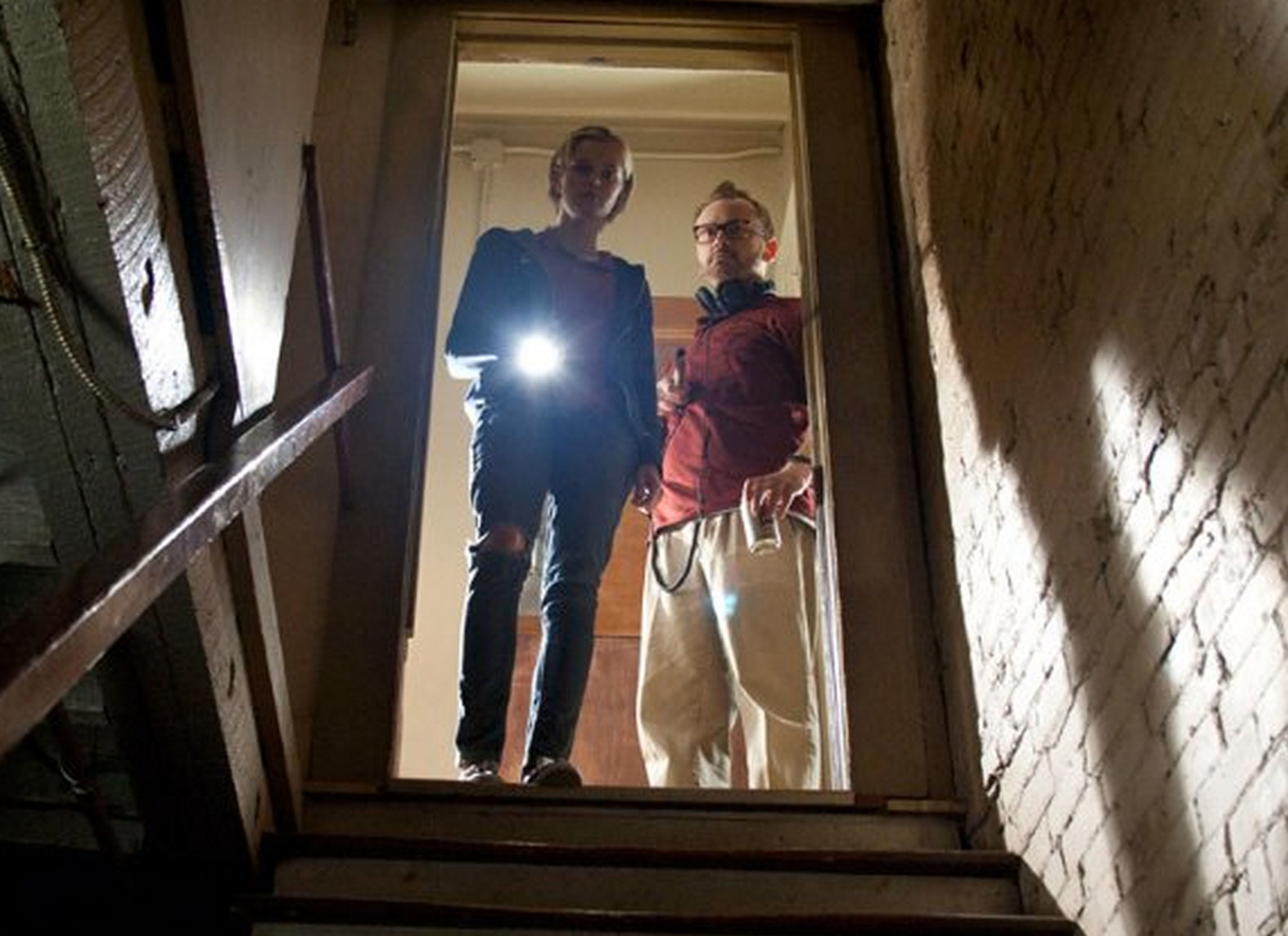 萨拉·帕克斯顿和帕特希利提高一个手电筒在黑暗的楼梯在“幽灵狩猎Innkeepers"