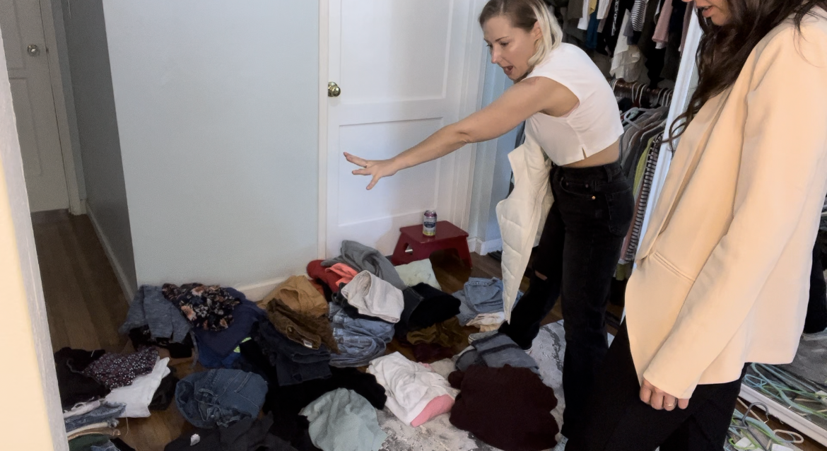 Two women standing in front of piles of folded clothing on the floor