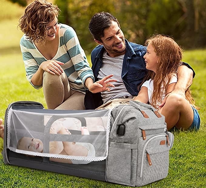 three people sitting around a backpack changing station with a baby inside