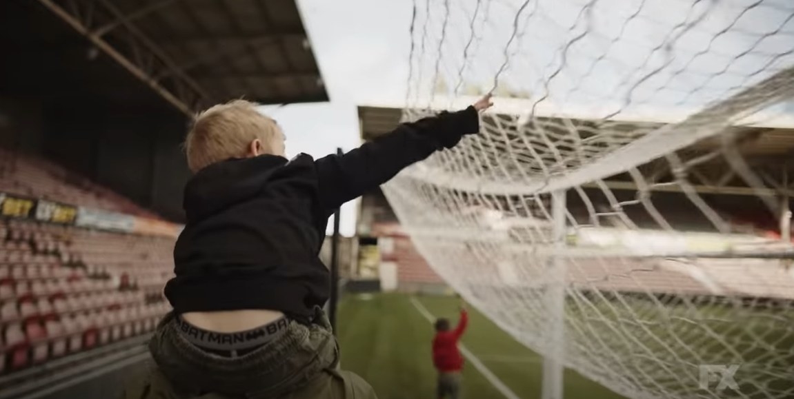 A child on his fathers shoulders touching the back of goals net