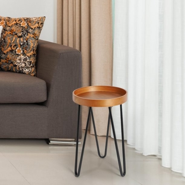 A wooden accent table with black legs by a grey couch