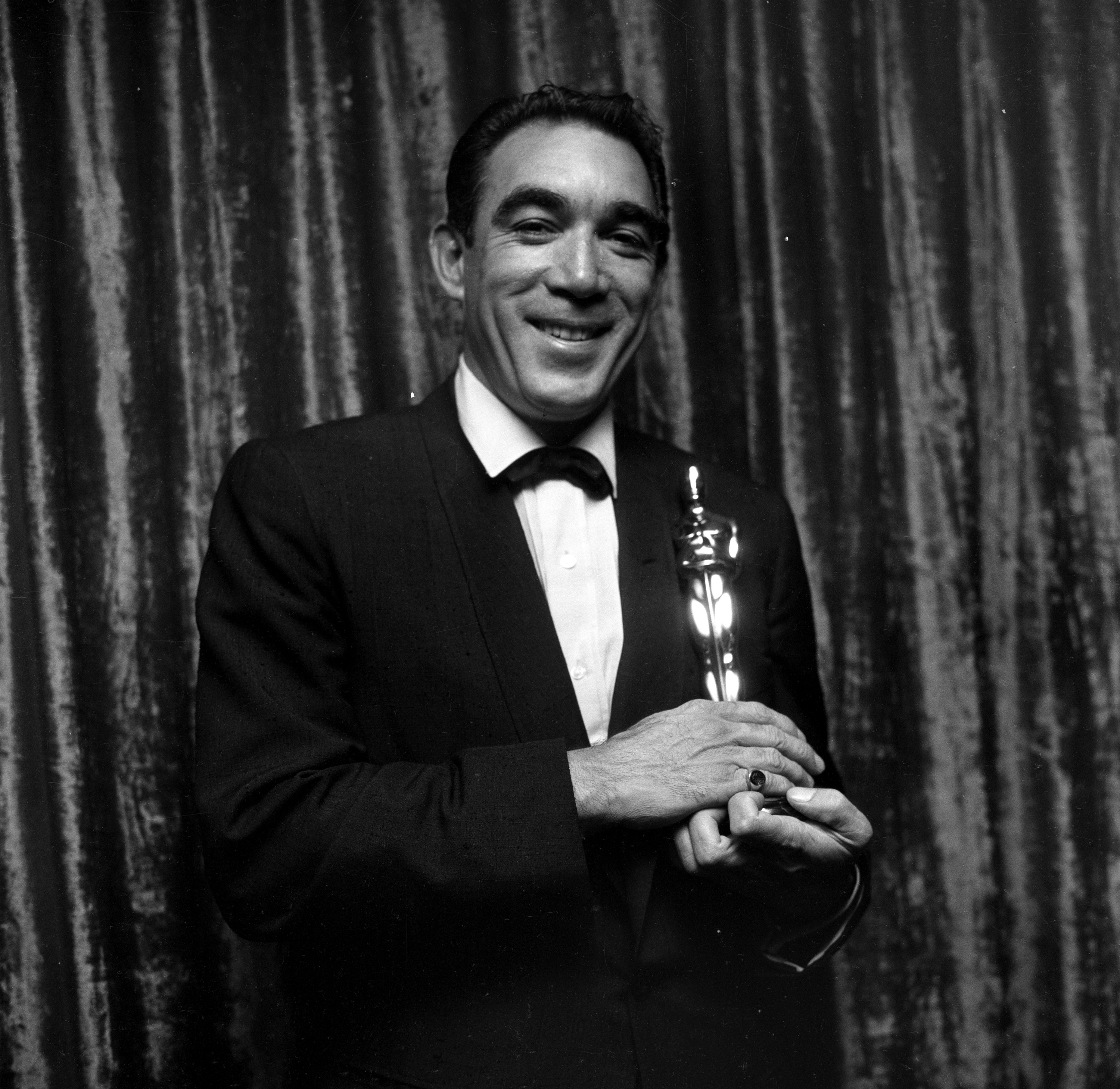 Anthony Quinn smiles while holding his Oscar at the 1957 Academy Awards