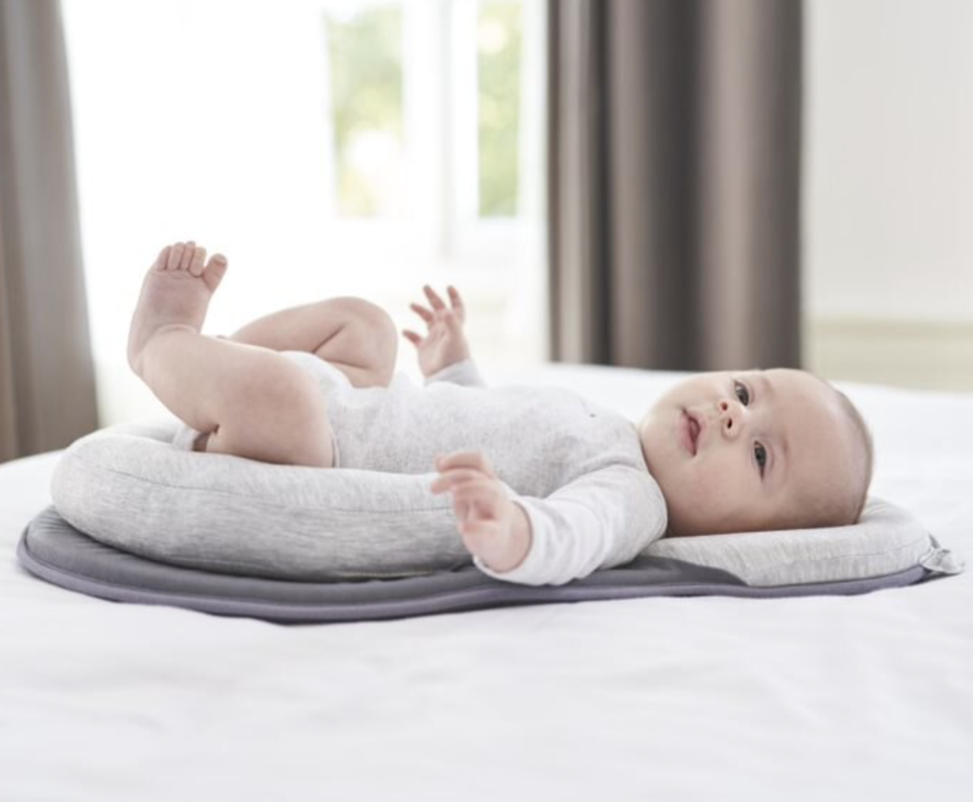 a baby lying in the padded baby lounger which is on a bed