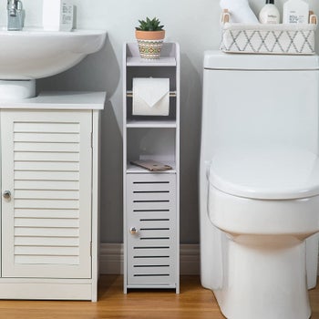 Light grey toilet paper holder in between a sink and a toilet.