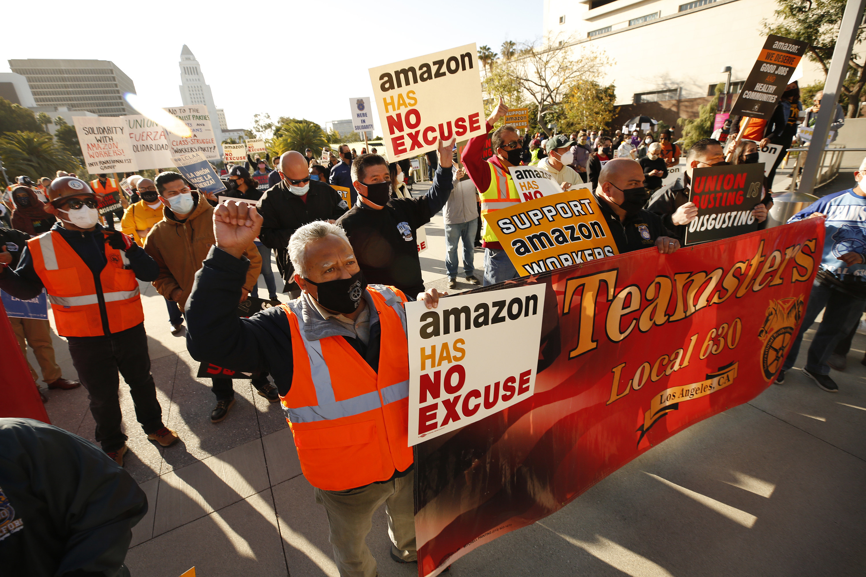Demonstrators hold up a large banner, signs reading &quot;Amazon has no excuse,&quot; and raise their fists in a protest