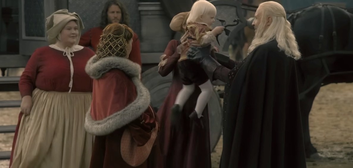 A woman hands Aegon to Viserys while a pregnant Alicent looks on