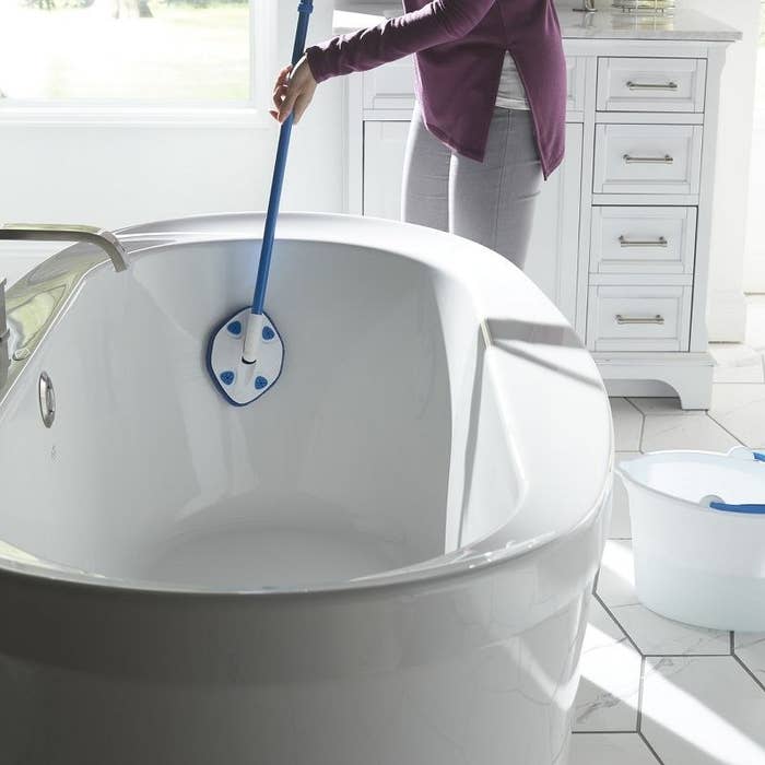 Model using blue extendable clorox tub cleaning wand to clean white porcelain tub