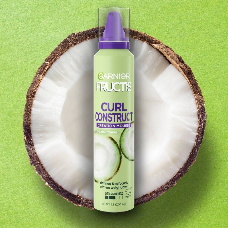 A bottle of hair mousse with half a sliced coconut