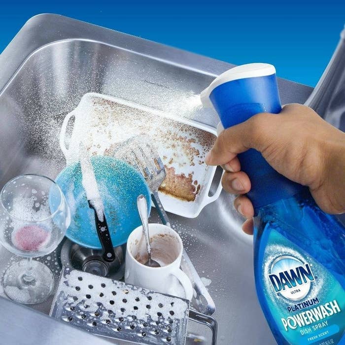 Model spraying blue bottle of Dawn Powerwash onto dirty dishes in sink