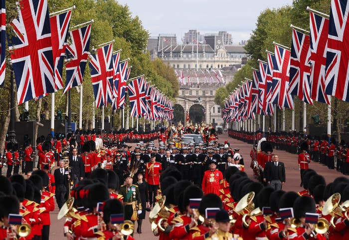 A crowd of buckingham palace guards in a uk-flag adorned caravan for the queen&#x27;s funeral