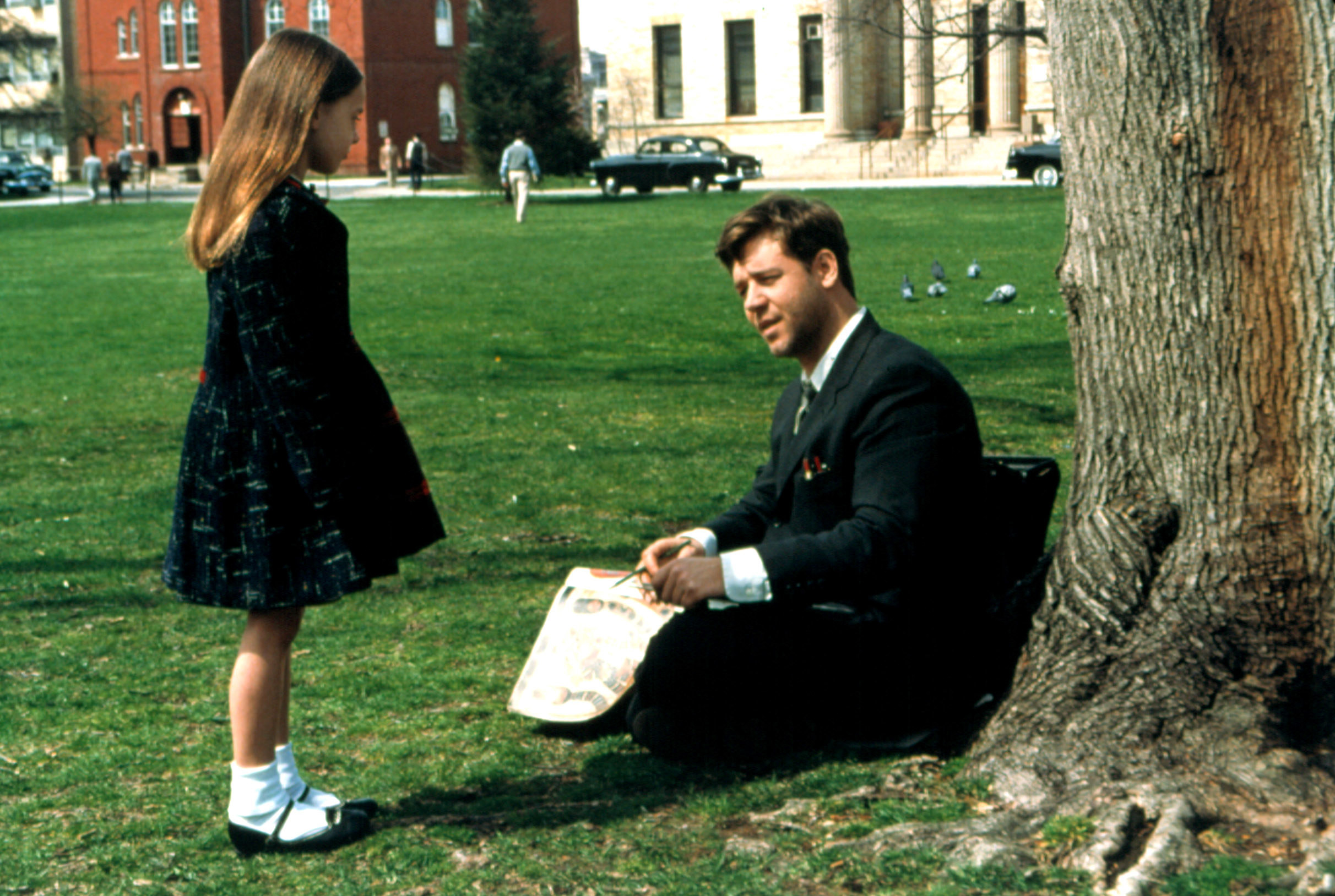 A little girl speaks to a man, who is sitting under a tree reading