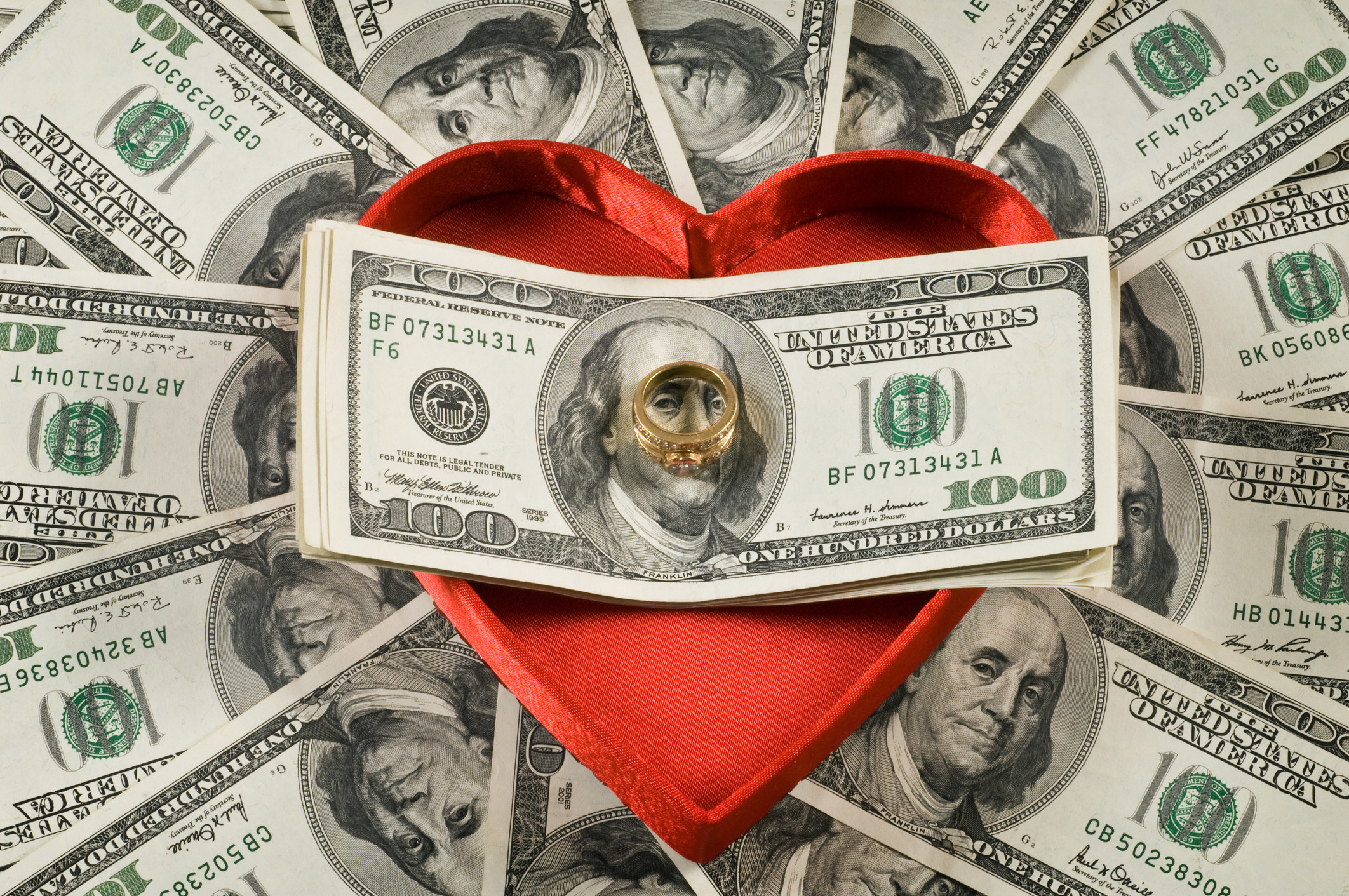A ring sitting on a stack of bills over a red heart