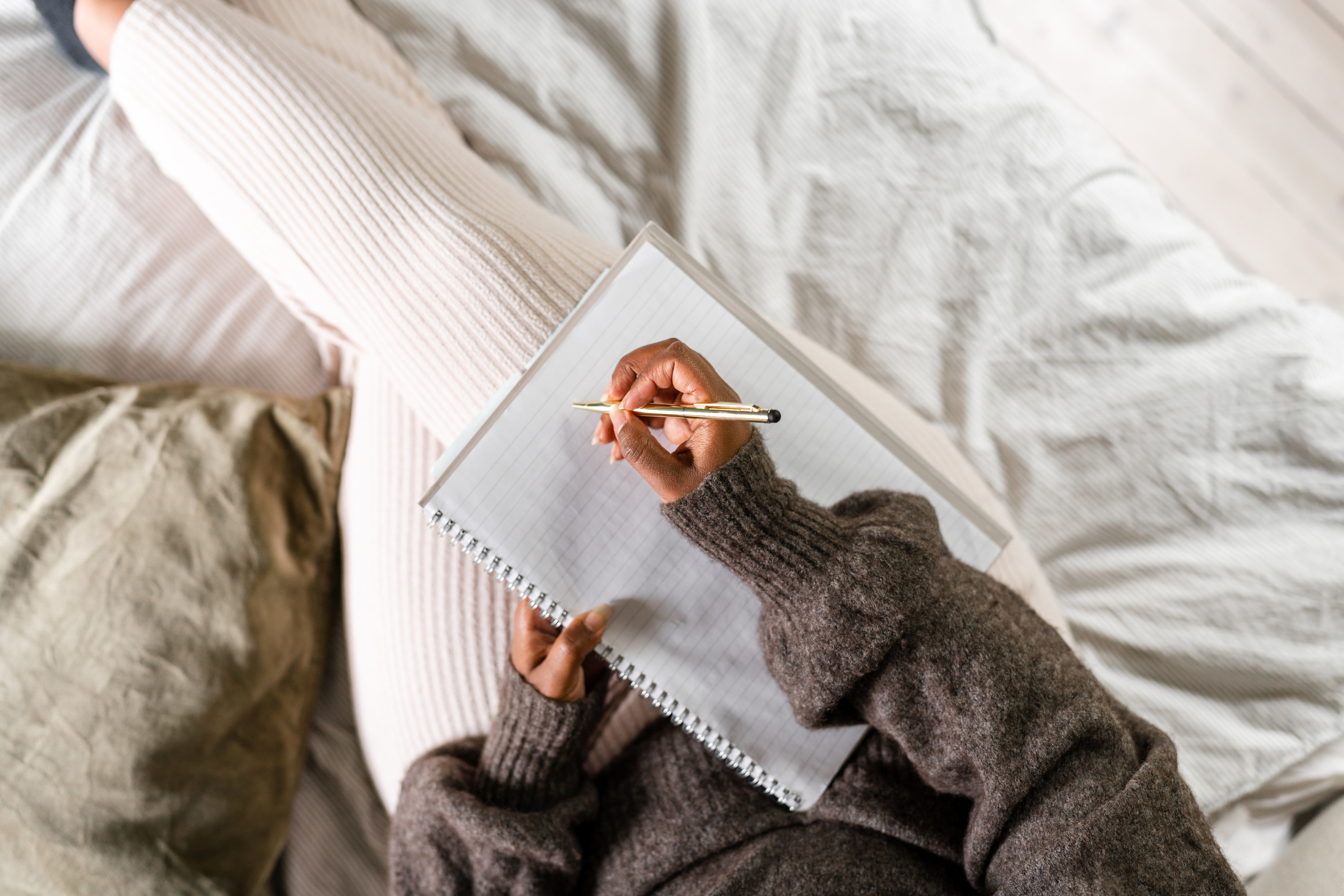 a woman sitting on the bed writing on a notebook