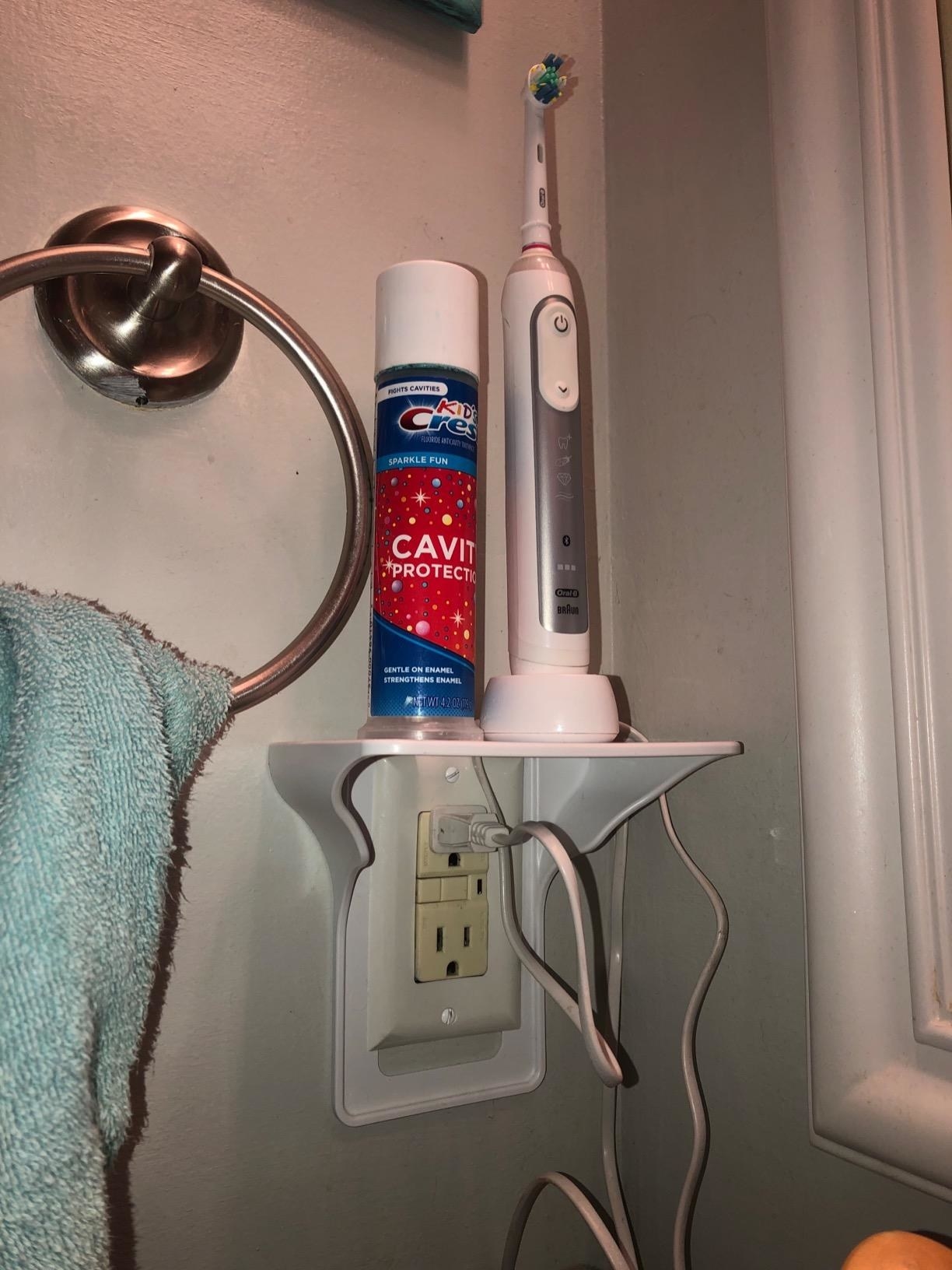 reviewer pic of outlet shelf with an electric toothbrush and toothpaste stored on it