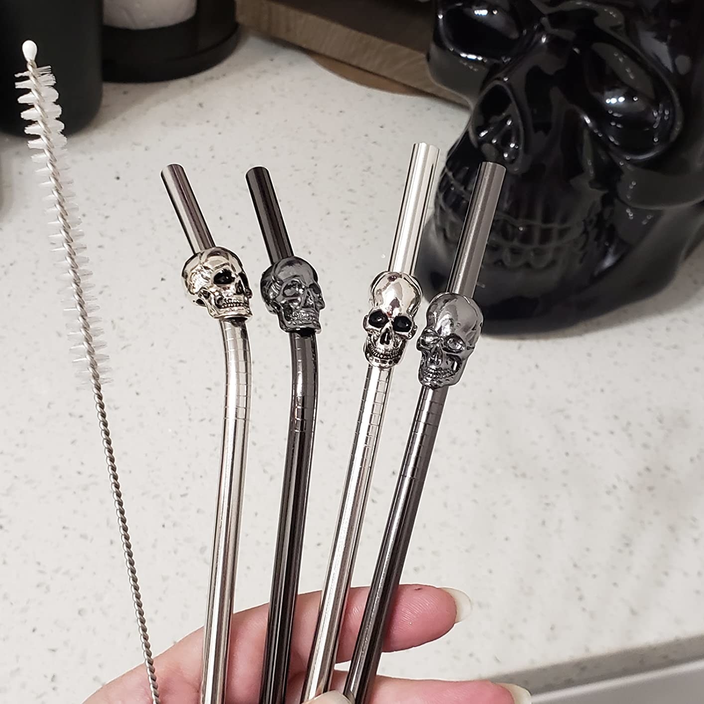Reviewer holds up four metal reusable skull straws and the cleaner pipe it comes with