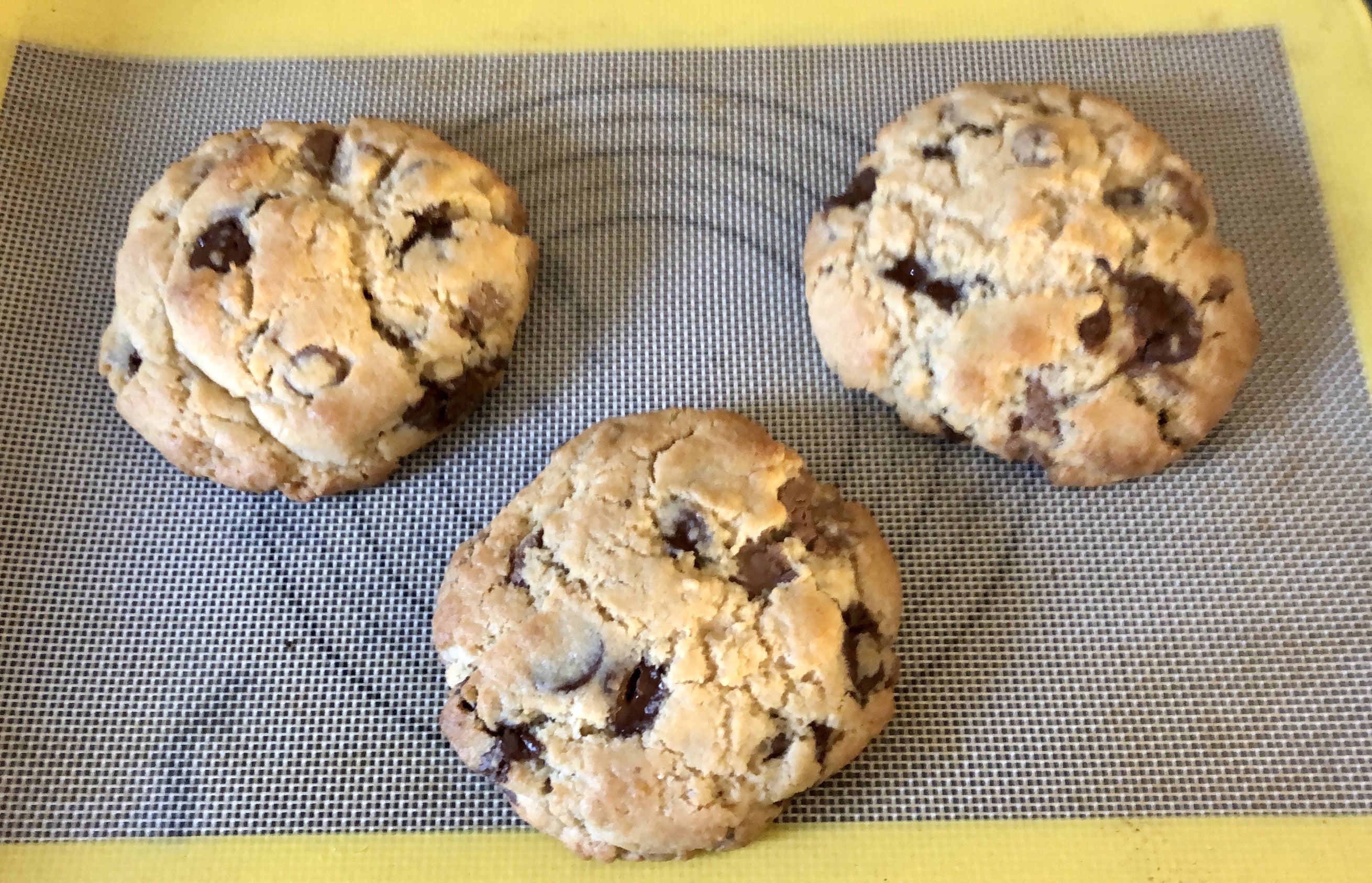 three large chocolate chips cookies on a yellow and tan silicone baking mat