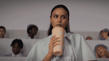 a girl drinking from a tumbler in class and looking amused