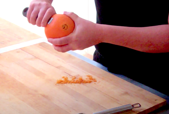 zesting an orange over a wooden cutting board