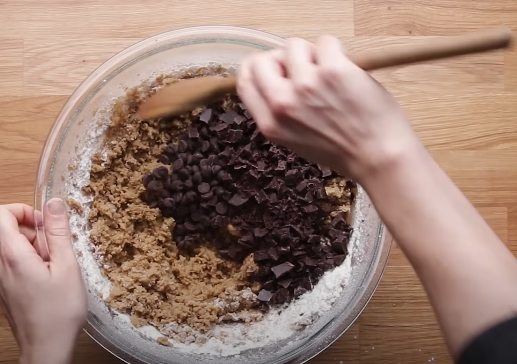Someone mixing chocolate chips and other ingredients in a bowl