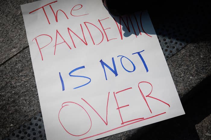 A protest sign on the ground reads &quot;THE PANDEMIC IS NOT OVER&quot; in red and blue ink