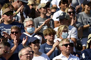 2021年9月11日，在宾夕法尼亚州大学公园的比弗体育场，两名宾夕法尼亚州立大学的球迷戴着口罩，看台上的球迷没有戴口罩，他们正在观看鲍尔州立红雀队对阵宾夕法尼亚州立大学尼塔尼狮子队的比赛。