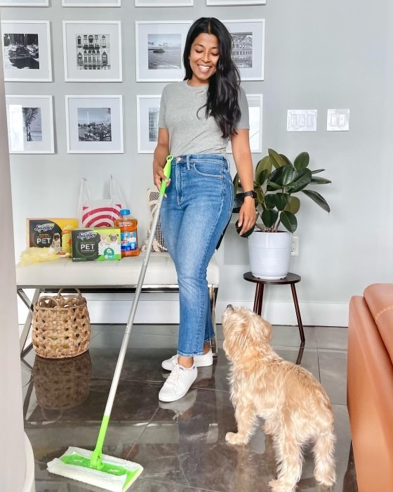 a model using the Swiffer to wipe the floor while standing by a dog