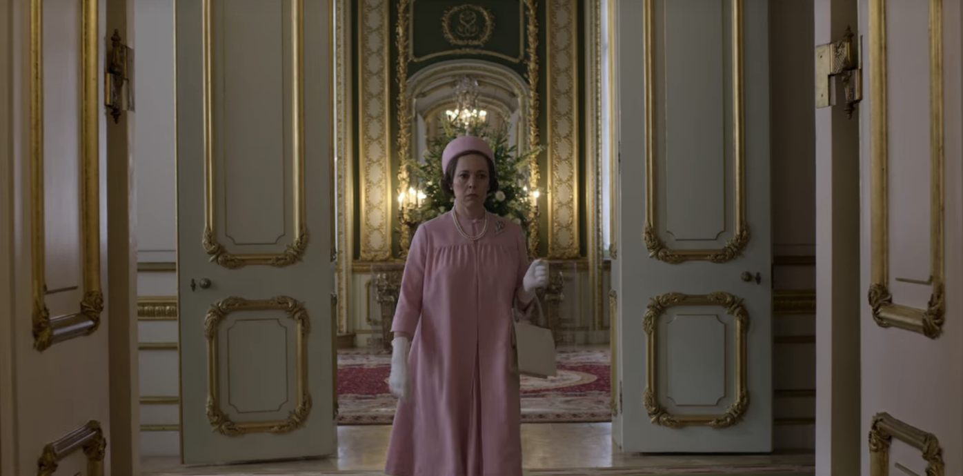 Olivia Colman in a similar pink outfit walking through the doors of the palace
