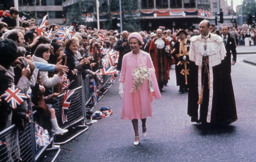 the queen walking by crowds of people and smiling in a knee-length pink dress