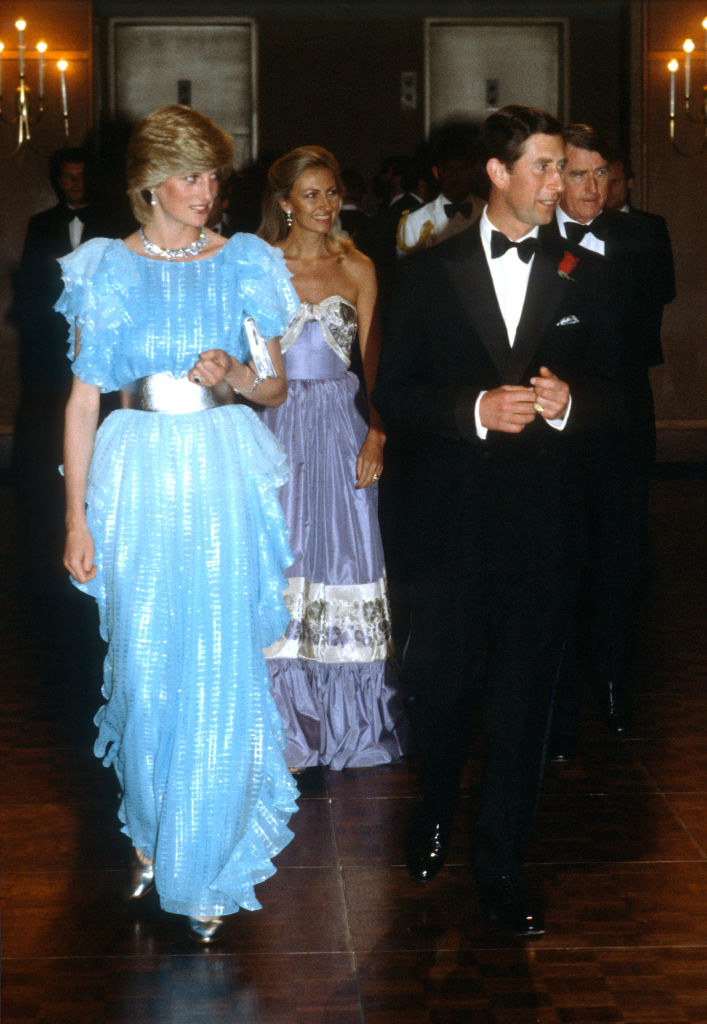 Princess Diana in a blue shimmery belted gown, walking with Prince Charles