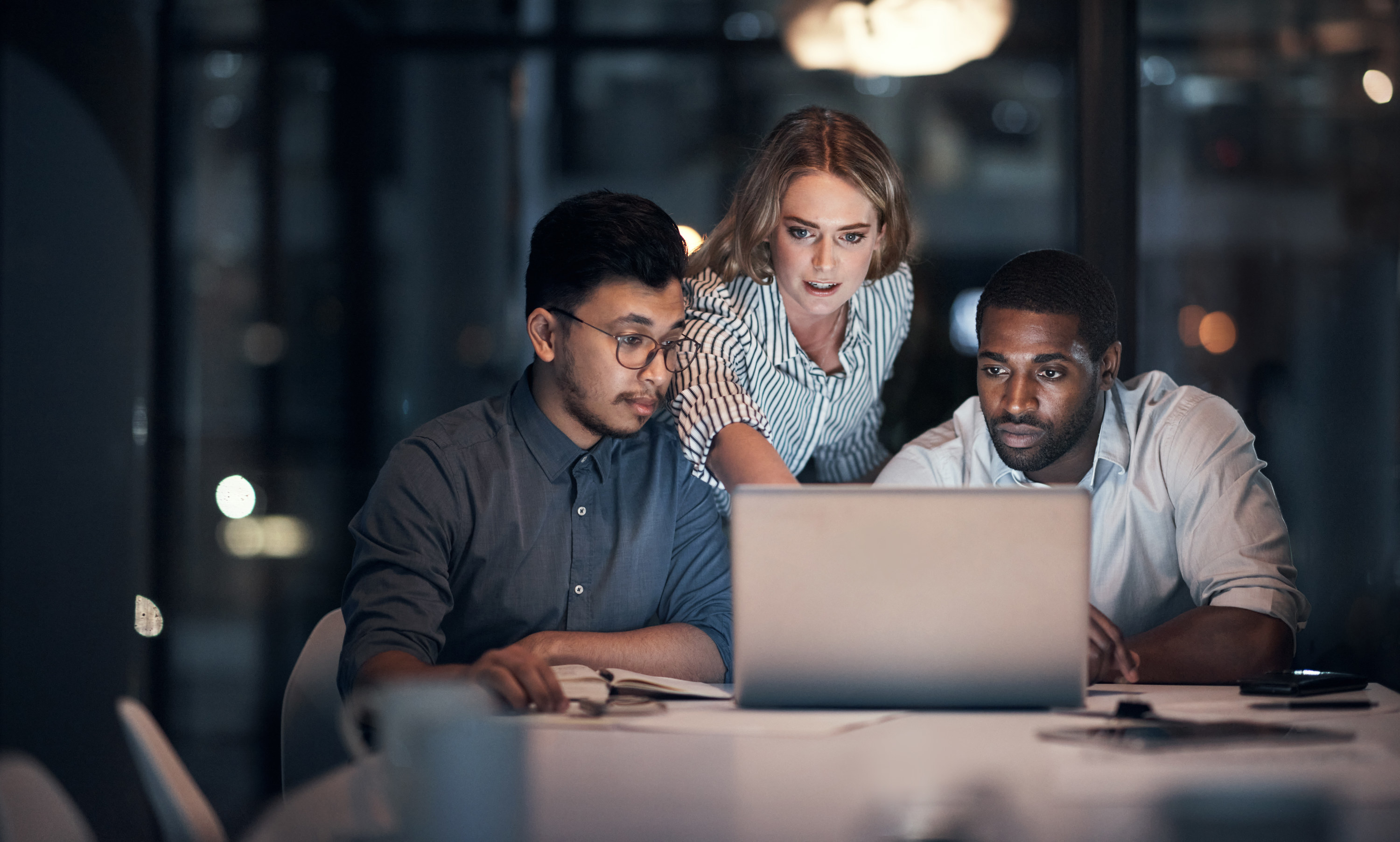 A woman points something out on a computer as she and two men look at the screen